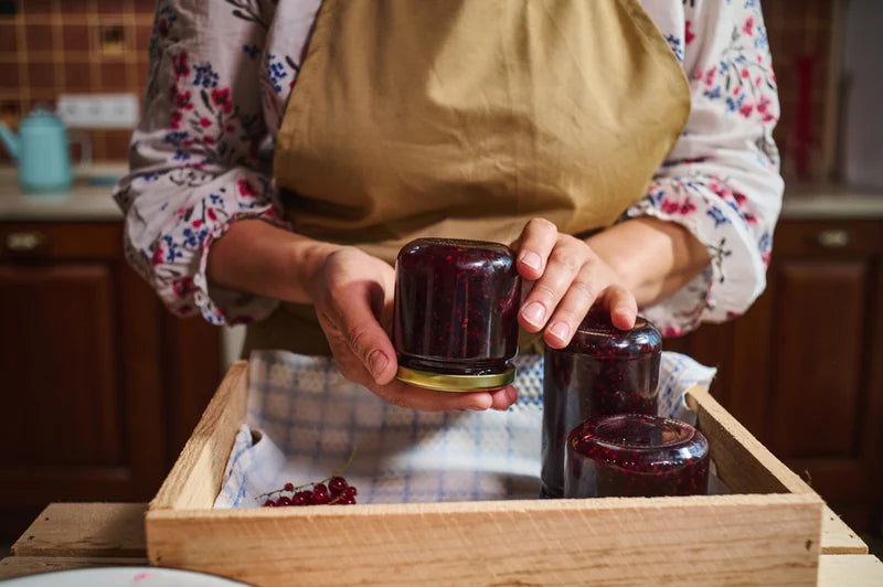 Person in an apron placing artisanal berry jam jars into a wooden crate.